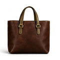 A dark brown leather tote bag with olive green handles and gold-tone buckle details, shown against a plain white background.